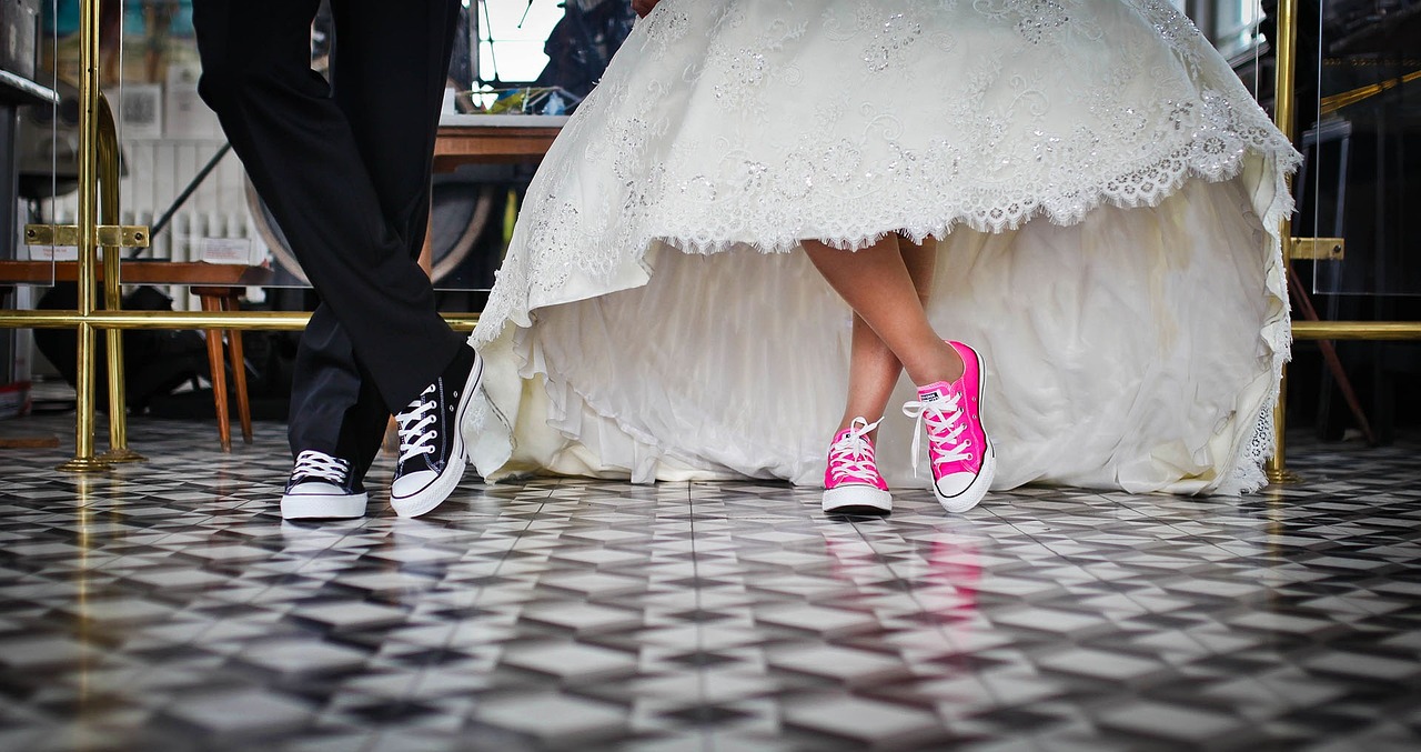 and groom standing before a courthouse, both dressed in formal attire and holding hands, a bouquet of flowers, and a stack of paperwork